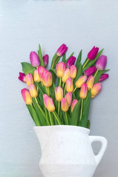 Bouquet of chic multi-colored tulips in an old jug on a gray background. The view from the top. Mother\'s day gift. Flat lay