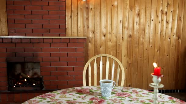 Una taza de té y una vela encendida en una mesa. Sillas de madera. Mantel con flores. Habitación interior . — Vídeo de stock