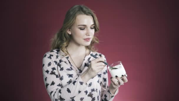 Attraktive junge Frau isst Joghurt und lächelt im Studio vor rotem Hintergrund. — Stockvideo