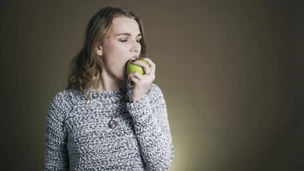 Jonge vrouw bijten en smakelijke groene appel eten. Over gouden achtergrond — Stockvideo