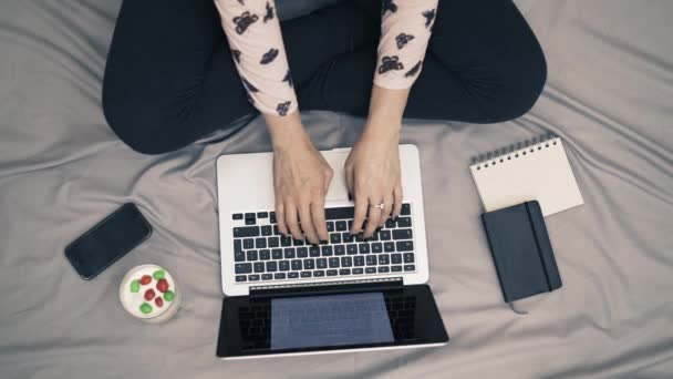 Vista dall'alto della donna a letto, piedi, laptop, yogurt e notebook sulla coperta grigia — Video Stock