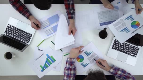 Three businesspeople discussing graphs, a colleague joins. Top view. — Stock Video