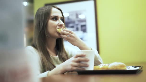 Вид сбоку женщины, которая ест пончик в кафе — стоковое видео