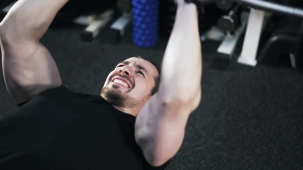 Pan shot van een man in het zwart is liggend op een bankje en doet een barbell oefening — Stockvideo