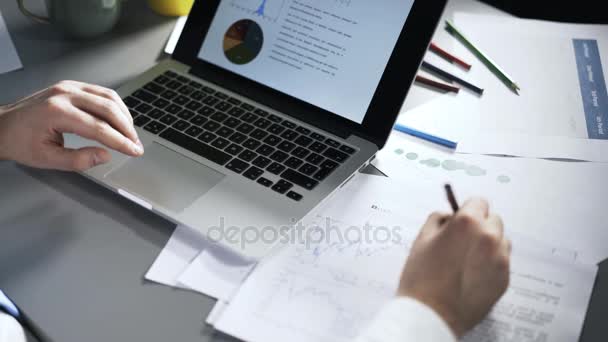 Top view of man looking at graphs on laptop and writing — Stock Video