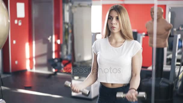 Bir spor salonunda dumbbells ile egzersiz genç sarışın kadın — Stok video
