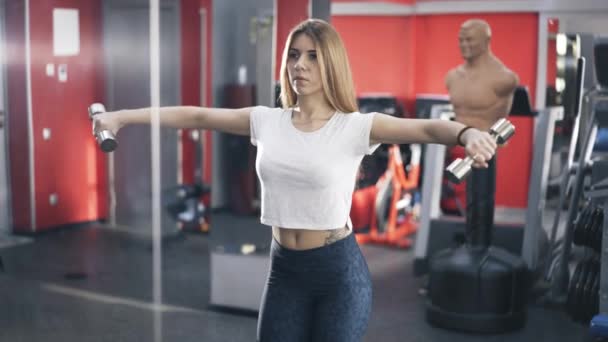 Mujer rubia haciendo lado mancuerna plantea en un gimnasio — Vídeo de stock