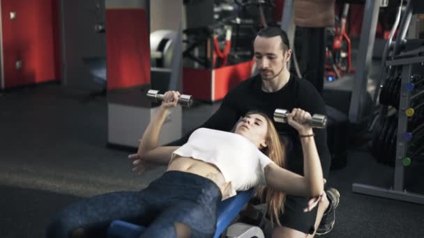Kadın bankta bir dumbbell egzersiz yapmak için yardımcı antrenör — Stok video
