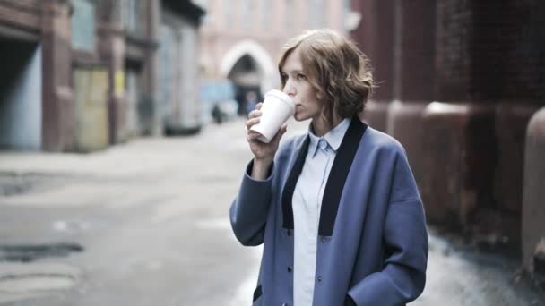 Mujer de negocios con abrigo azul bebiendo café afuera — Vídeos de Stock