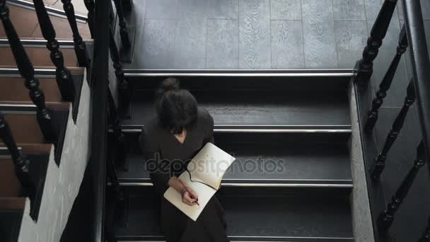 Vista superior de una joven escribiendo en cuaderno en las escaleras — Vídeo de stock