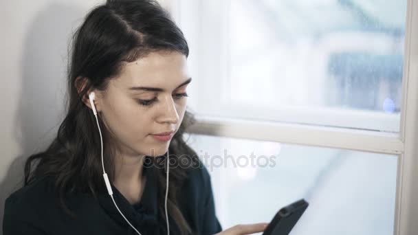 Mujer está escuchando música en los auriculares y mirando a la cámara — Vídeo de stock