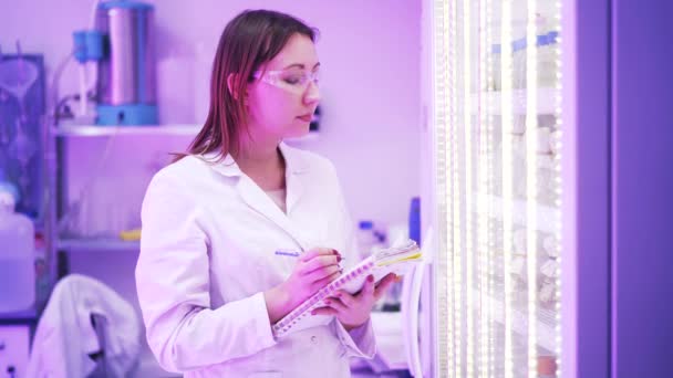 Femme scientifique prenant des notes près d'un placard avec des flacons — Video