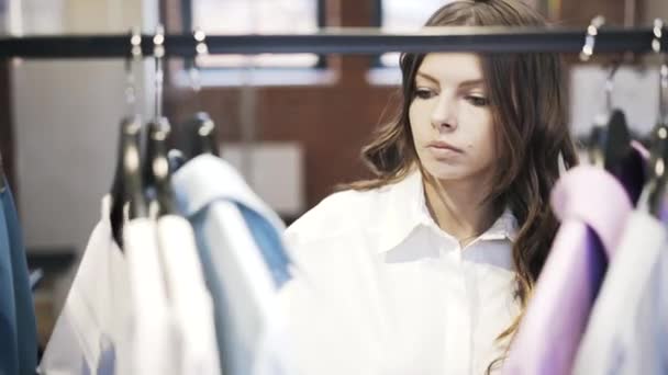 Joven hermosa mujer eligiendo ropa en una tienda, vista frontal — Vídeos de Stock