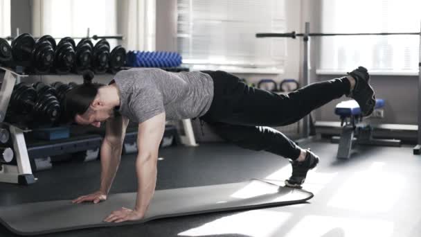 Junger muskulöser Mann beim Einbeinplanken in einem Fitnessstudio — Stockvideo