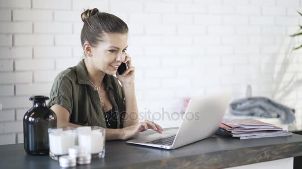 Mujer joven hablando por teléfono y utilizando el ordenador portátil — Vídeo de stock