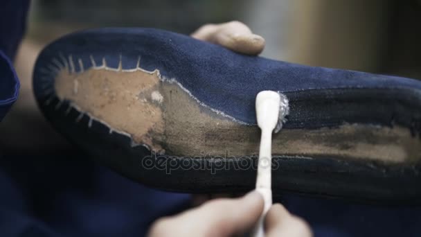 Cobbler aplicando pegamento a una suela de zapato azul con un cepillo, de cerca — Vídeos de Stock