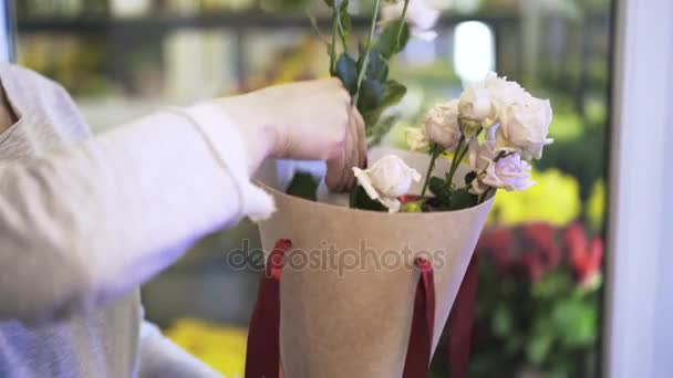Primer plano de las manos de la florista mujer poniendo rosas en una caja cónica — Vídeos de Stock