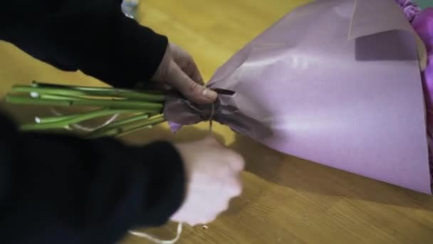 Zijaanzicht van vrouw s handen een roze bloemboeket te verpakken in een winkel — Stockvideo