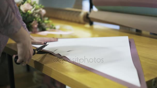 Floristería s manos cortando papel de embalaje en su mesa — Vídeos de Stock