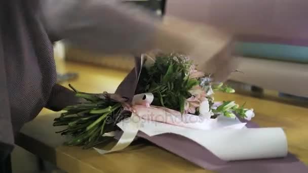 Флорист, обмотуючи купу квітів, прив'язаних стрічкою на її столі — стокове відео