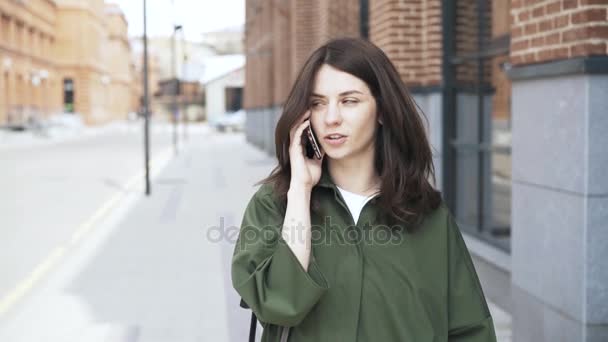 Милая девушка в зеленой рубашке разговаривает по телефону на улице, вид спереди — стоковое видео