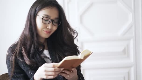 Ung asiatisk kvinna läser en liten orange bok hemma — Stockvideo