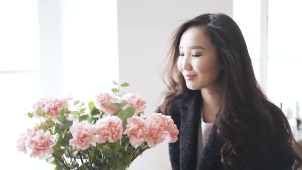 Young Asian woman smelling a pink flower in a vase at home — Stock Video