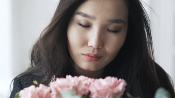 Asian young woman is smelling carnations and looking at you with desire — Stock Video