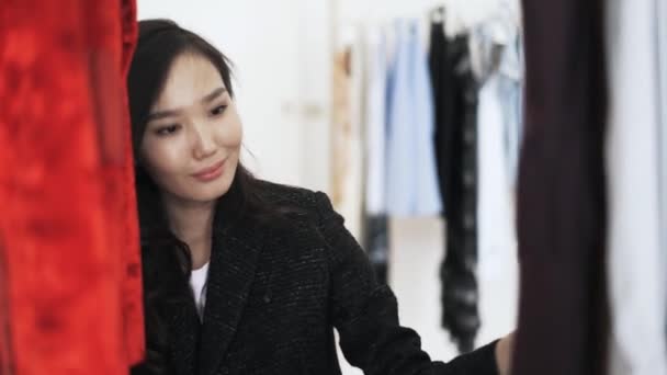 Attraktiva asiatisk ung kvinna att välja en klänning i en affär — Stockvideo