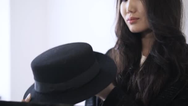 Asijské žena v plášti se snaží na klobouk v obchodě — Stock video