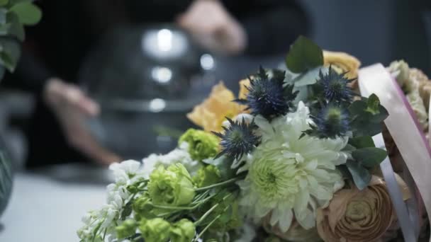 Женщина-флористка чистит стеклянную вазу на заднем плане, цветочный букет — стоковое видео