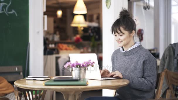 Young woman in a gray sweater smiling and web surfing in a cafe — Stock Video