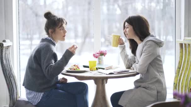 Dos jóvenes estudiantes universitarias comiendo en un café y hablando — Vídeos de Stock