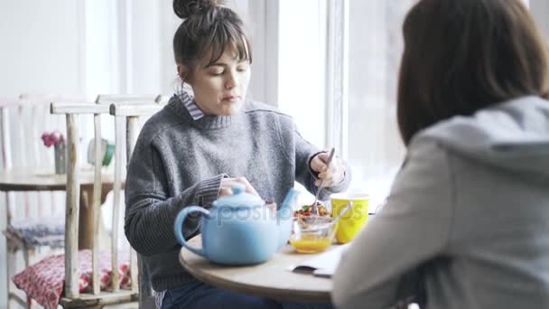 Due giovani studentesse che mangiano in un caffè e parlano, si inclinano — Video Stock