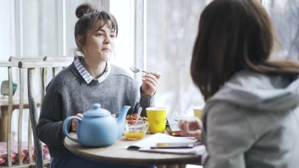 Dos jóvenes estudiantes de la universidad comiendo en un café y hablando, lado — Vídeo de stock