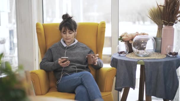 Hermosa joven escuchando música en un sillón — Vídeos de Stock