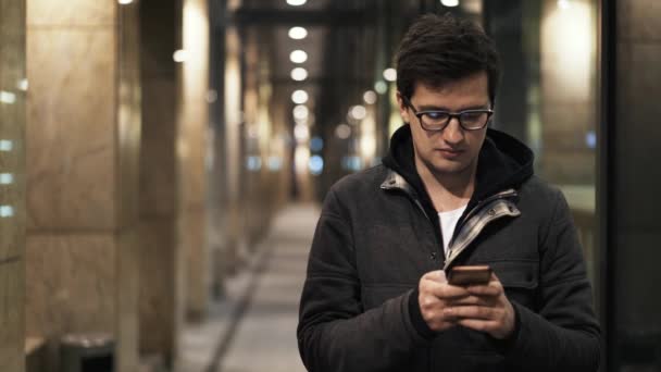 メガネの若い男は、夜の通りでテキスト メッセージ — ストック動画