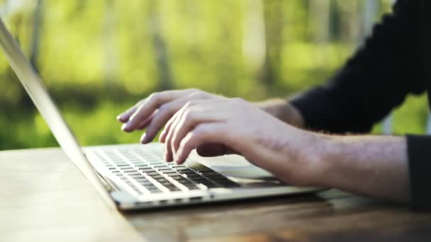 Homme tapant au clavier de l'ordinateur portable dans un parc gros plan — Video