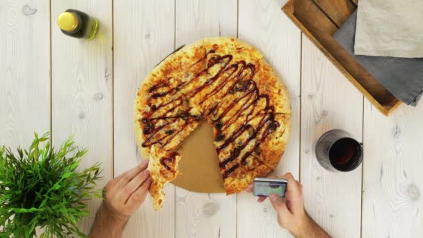 Вид сверху на человека, который ест пиццу и пользуется смартфоном — стоковое видео