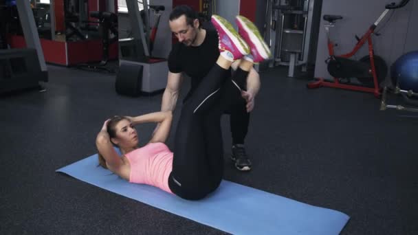 Mujer en rosa haciendo levantamientos de piernas con un entrenador personal — Vídeos de Stock