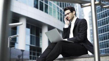 Bir dizüstü bilgisayar ile oturma ve dışındaki telefon konuşurken işadamı