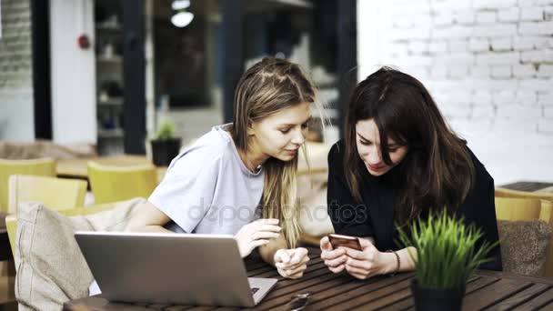 Twee vriendinnen zijn zitten in een cafe en kijken naar een smartphone — Stockvideo