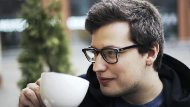 Крупный план парня в очках, пьющего кофе, слушающего друзей и смеющегося — стоковое видео