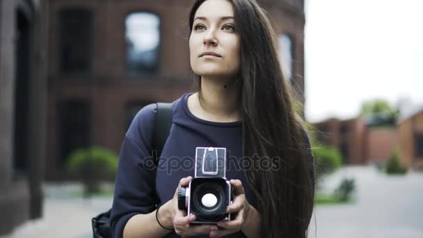 Beautiful black haired girl is holding an old fashioned camera in the street — Stock Video