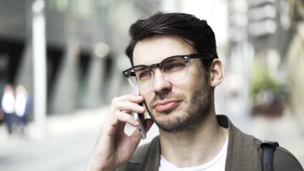 Vista frontal de un tipo hipster en gafas hablando por teléfono y riendo afuera — Vídeos de Stock