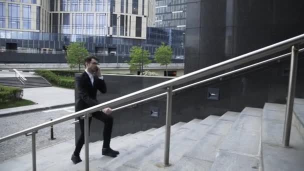 Junger Geschäftsmann mit Brille, der nach oben geht und telefoniert, Seitenansicht — Stockvideo