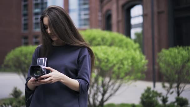 Mujer joven en un suéter azul se divierte con una vieja cámara afuera — Vídeos de Stock