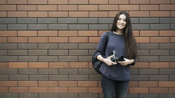Mujer joven con una cámara antigua cerca de una pared de ladrillo — Vídeos de Stock