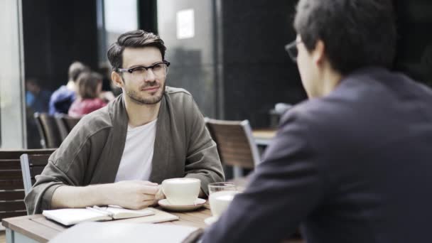 2 つの流行に敏感な若い男は、屋外のカフェで会話します。 — ストック動画