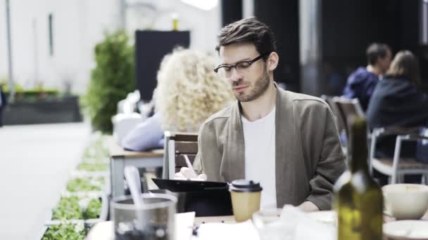 Молодий чоловік в окулярах ескіз в кафе зовні — стокове відео
